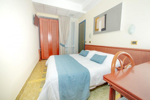 Mały pokój hotelowy z łóżkiem małżeńskim i drewnianymi meblami.