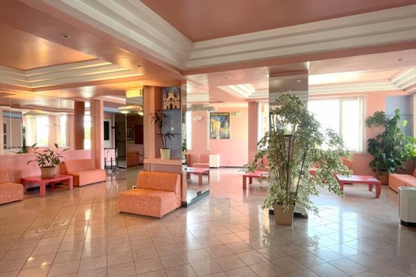 Jasne oświetlone lobby hotelowe z różowymi sofami, dużymi roślinami i lustrami.