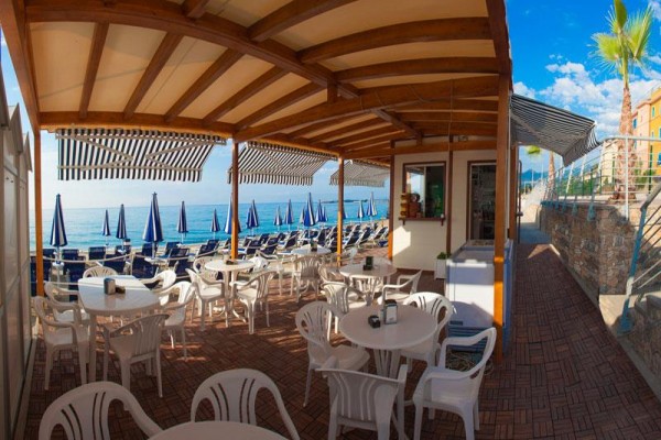 Otwarty taras restauracji z widokiem na morze i plażę z niebieskimi parasolami.