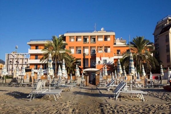 Czteropiętrowy budynek z pomarańczową fasadą i parasolami na piaszczystej plaży.