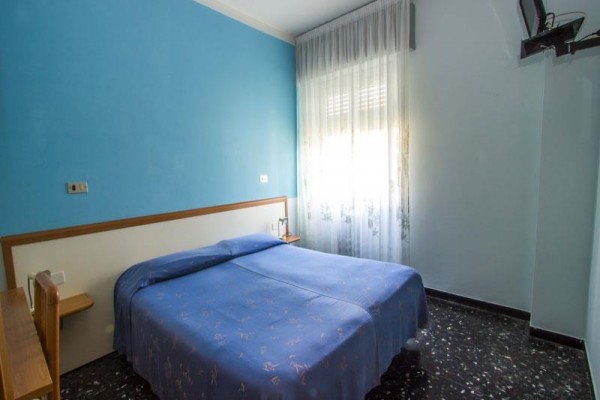 Pokój z niebieską ścianą i podwójnym łóżkiem pod oknem.