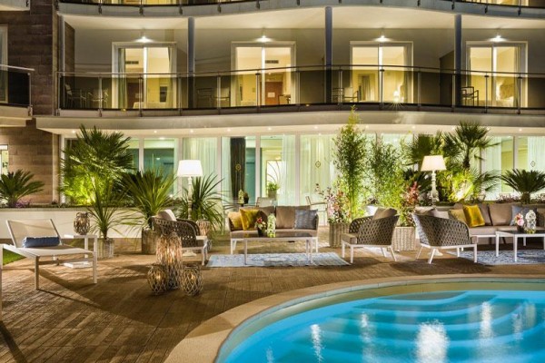 Hotelowy taras z podświetlanym basenem i miejscem do siedzenia otoczonym roślinami wieczorem.