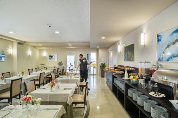 Restauracja z obrusami na stołach i bufetem, gdzie obsługa poprawia stół.