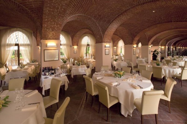 Elegancka restauracja z sklepionym ceglanym sufitem i okrągłymi stołami z białymi obrusami.