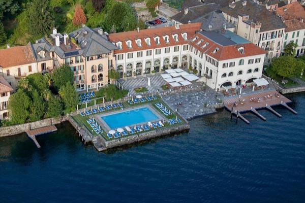 Hotel z basenem przy jeziorze otoczony zielenią.