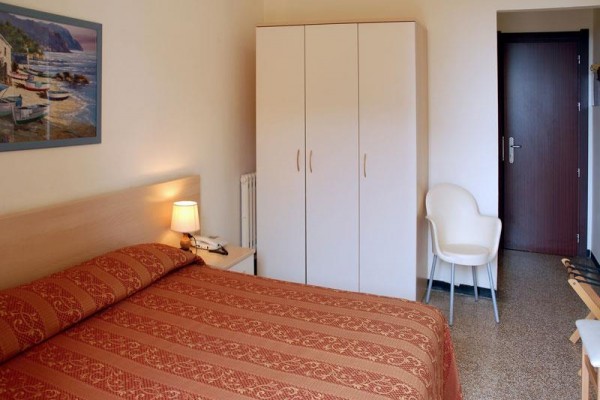 Pokój hotelowy z podwójnym łóżkiem, szafą, krzesłem i stolikiem nocnym z lampką.