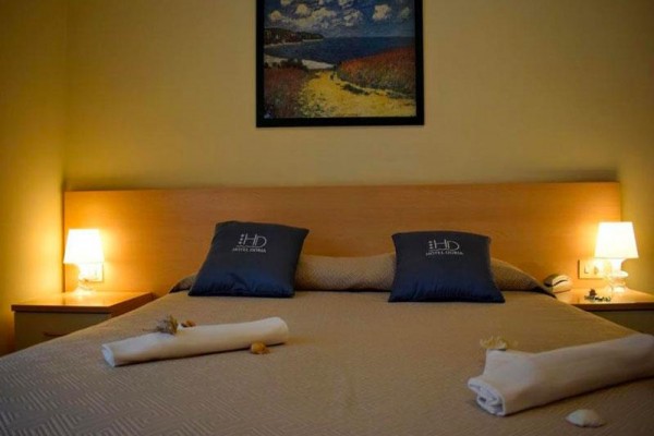 Łóżko w pokoju hotelowym z obrazem krajobrazu na ścianie i dwoma stolikami nocnymi z lampami.