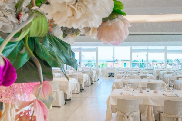 Elegancka restauracja z białymi obrusami i widokiem na zewnętrzny taras przez duże okna.
