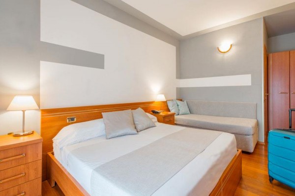 Nowoczesny pokój hotelowy z łóżkiem małżeńskim, sofą i niebieską walizką.