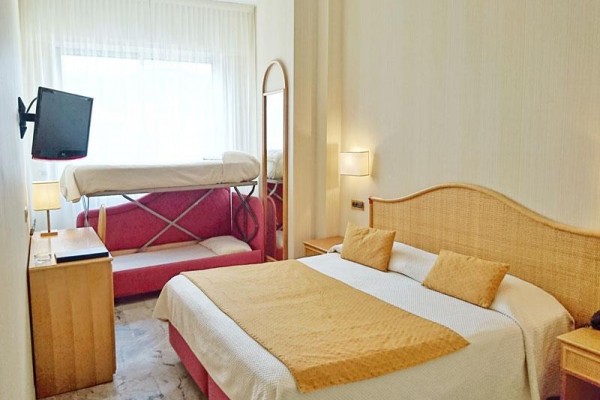 Pokój hotelowy z łóżkiem małżeńskim, piętrowym łóżkiem, telewizorem i oknem z białymi zasłonami.