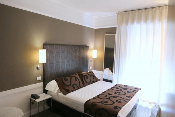 Pokój hotelowy z łóżkiem małżeńskim, udekorowany brązowymi narzutami i poduszkami.