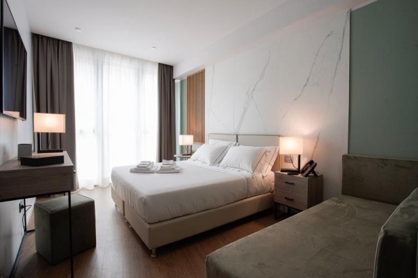 Nowoczesny pokój hotelowy z łóżkiem małżeńskim, stolikami nocnymi i lampkami.