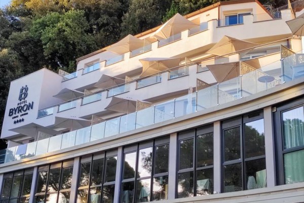 Nowoczesny hotel z tarasami i parasolami w górzystym otoczeniu.