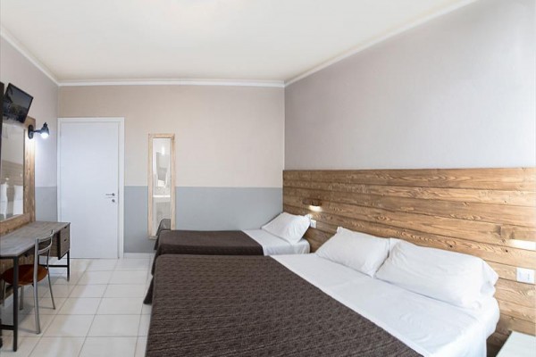 Pokój hotelowy z dwoma łóżkami małżeńskimi, stołem i telewizorem na ścianie.