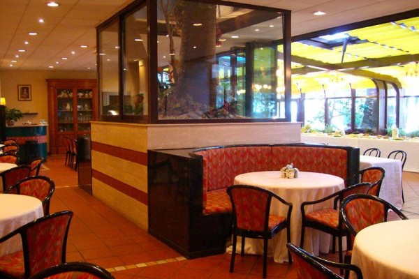 Restauracja z okrągłymi stolikami i czerwonymi krzesłami wokół akwarium pośrodku.