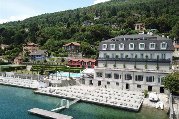 Hotel nad jeziorem otoczony zielonymi wzgórzami i innymi budynkami.