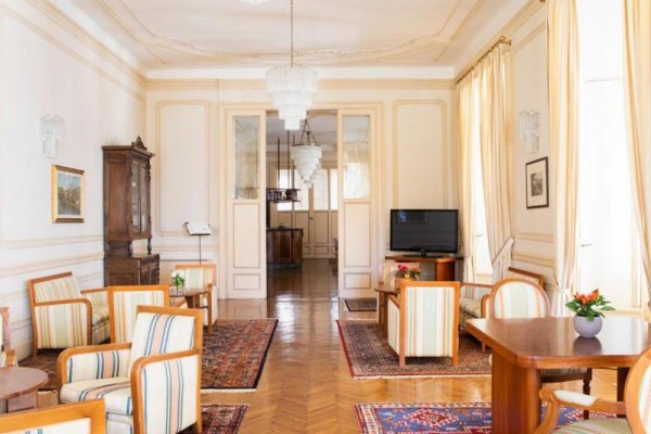Elegancki salon z drewnianą podłogą, pasiastymi fotelami i kryształowymi żyrandolami.