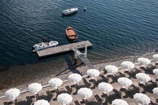 Widok z góry na plażę z rzędami białych parasoli i molo z łodziami na wodzie.