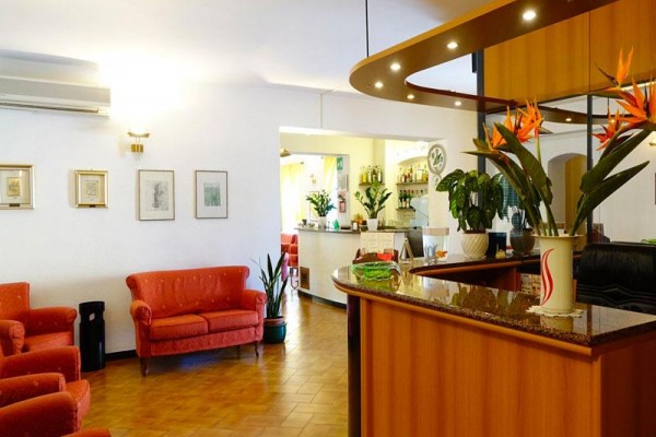 Recepcja hotelowa z drewnianym kontuarem, kwiatami i czerwonymi meblami.