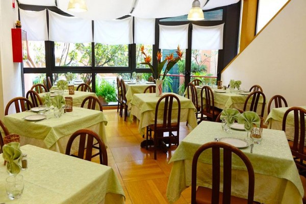 Wnętrze restauracji z drewnianymi krzesłami i obrusami w jasnym odcieniu zieleni.