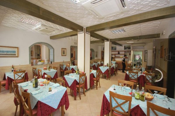 Restauracja z drewnianymi krzesłami i stołami przykrytymi niebieskimi obrusami.