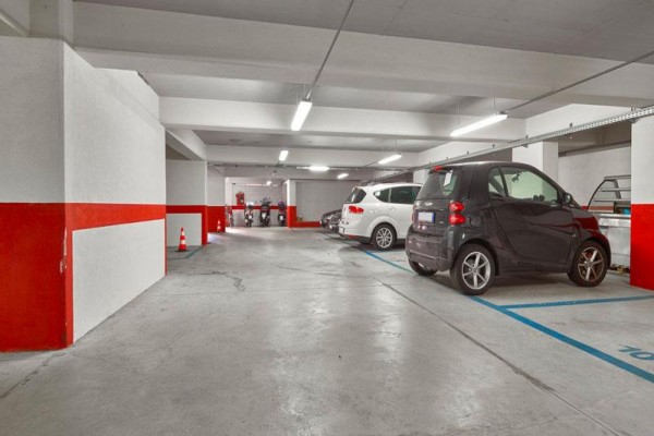 Podziemny parking z kilkoma zaparkowanymi samochodami i motocyklami.