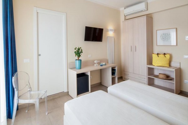 Jasny pokój hotelowy z dwoma łóżkami, biurkiem, telewizorem i szafą.  