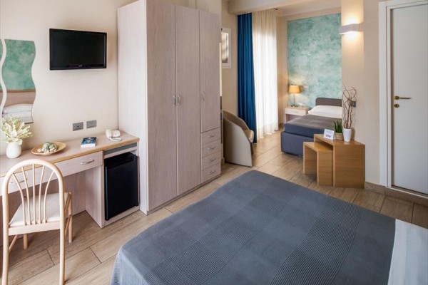 Przytulny pokój hotelowy z łóżkami, szafą, biurkiem i telewizorem na ścianie.