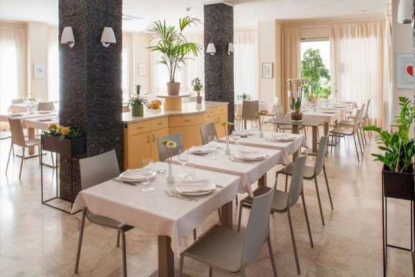 Nowoczesna restauracja z nakrytymi stołami i jasnym wnętrzem, ozdobiona roślinami.