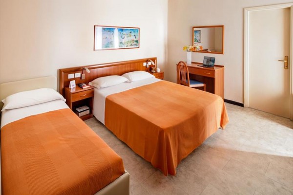Pokój hotelowy z dwoma łóżkami z pomarańczowymi narzutami i biurkiem.