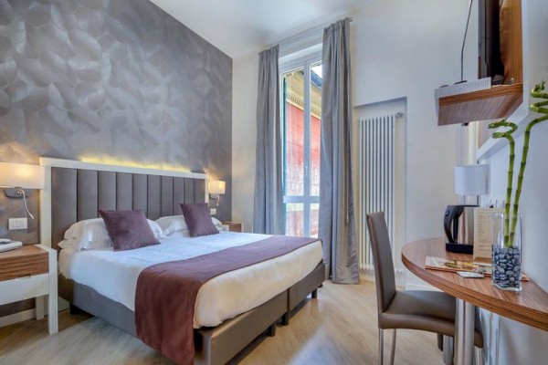Nowocześnie urządzony pokój hotelowy z łóżkiem małżeńskim, biurkiem i dużym oknem.