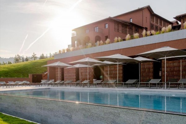 Luksusowy hotelowy basen z leżakami i parasolami przed budynkiem w zachodzącym słońcu.