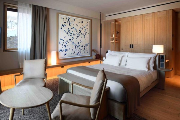 Luksusowy pokój hotelowy z dużym łóżkiem, drewnianymi meblami i nowoczesną sztuką na ścianie.