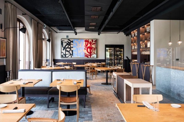 Nowoczesna restauracja z drewnianymi meblami i abstrakcyjnymi obrazami na ścianie.