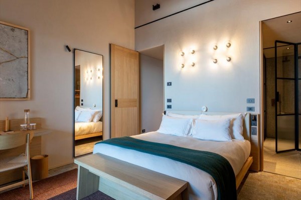 Nowoczesny pokój hotelowy z podwójnym łóżkiem, drewnianymi elementami i otwartą łazienką.