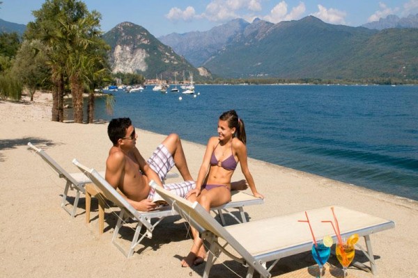 Dwie osoby leżą na plaży na leżakach z napojami nad morzem.
