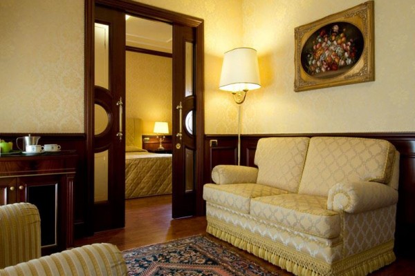 Elegancki salon z sofą, lampą i obrazem na ścianie, prowadzący do sypialni.