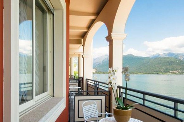 Balkon z łukami, stolikiem i kwiatem, widok na jezioro i góry.