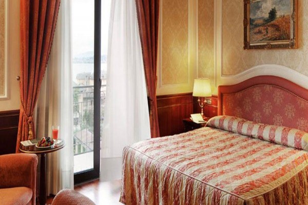 Luksusowy pokój hotelowy z łóżkiem małżeńskim, lampą, obrazem i balkonowym widokiem na jezioro.