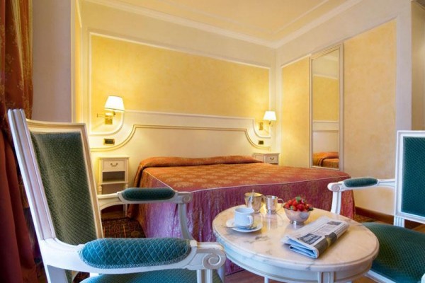 Elegancki pokój hotelowy z podwójnym łóżkiem, stołem, fotelami i filiżanką kawy.