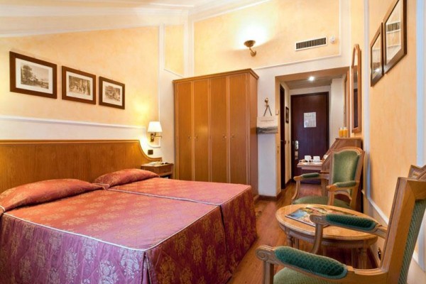 Pokój hotelowy z dwoma połączonymi łóżkami, szafą i krzesłami.