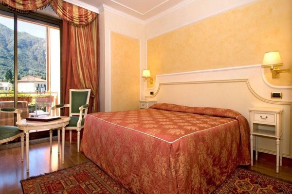 Elegancki pokój hotelowy z łóżkiem małżeńskim i balkonem z widokiem na góry.