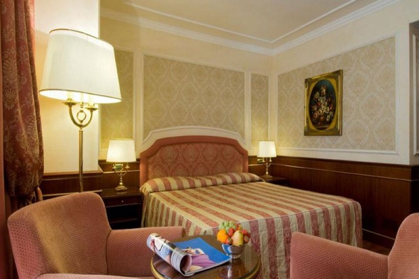 Pokój hotelowy z łóżkiem małżeńskim, dwiema lampami i owocami na stole.