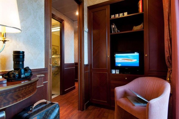 Luksusowy pokój hotelowy z telewizorem, aparatem fotograficznym na stole i otwartą walizką na podłodze.