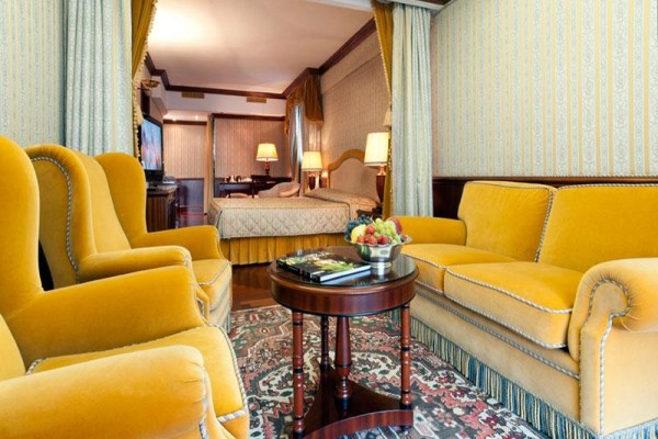 Elegancki pokój hotelowy z żółtymi tapicerowanymi meblami i stolikiem kawowym z owocami.