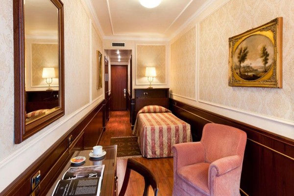 Elegancki pokój hotelowy z łóżkiem pojedynczym, fotelem i filiżanką kawy na stole.