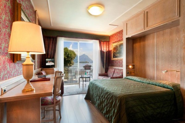 Elegancki pokój hotelowy z widokiem na jezioro i góry przez przeszklone drzwi na taras.
