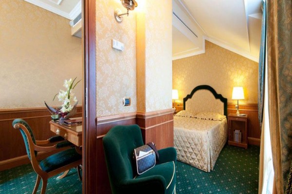 Luksusowy pokój hotelowy ze złotym wystrojem i podwójnym łóżkiem obok biurka z zielonym fotelem.