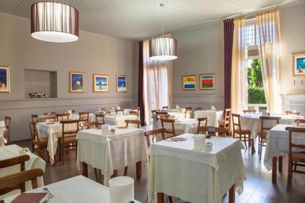 Restauracja z drewnianymi krzesłami i stołami pokrytymi białymi obrusami, z obrazami na ścianach.