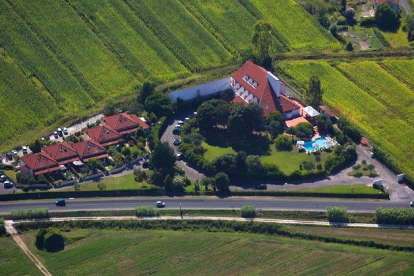Widok z lotu ptaka na kompleks budynków z czerwonymi dachami otoczony zielonymi polami.